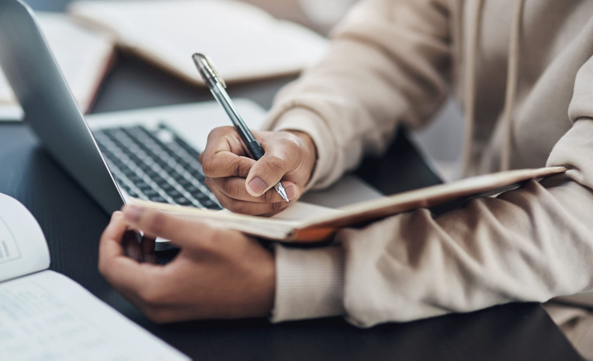 a human torso writing in a notebook next to a laptop