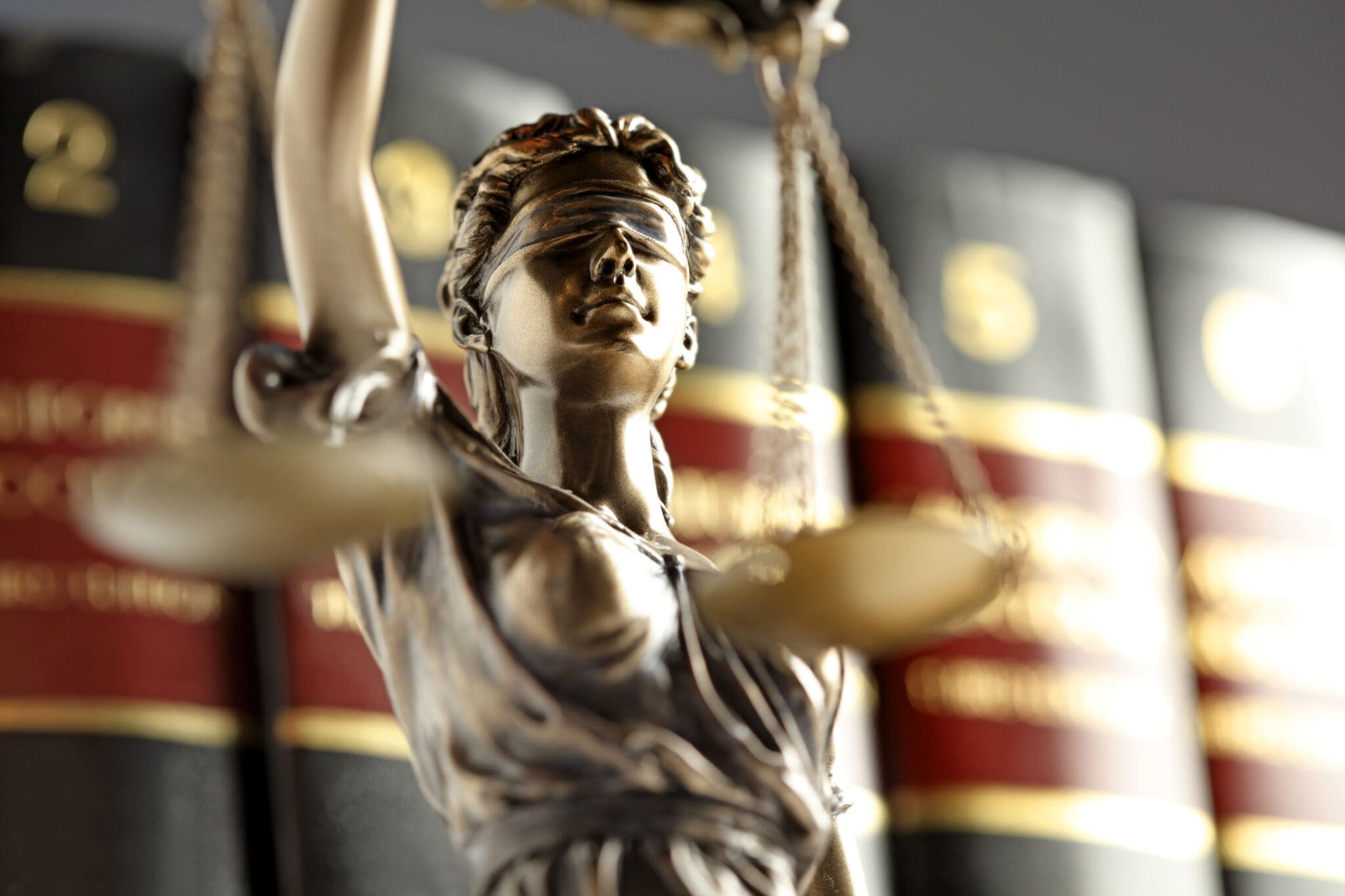 A close up of the statue of lady justice standing in front of an out of focus row of law books.