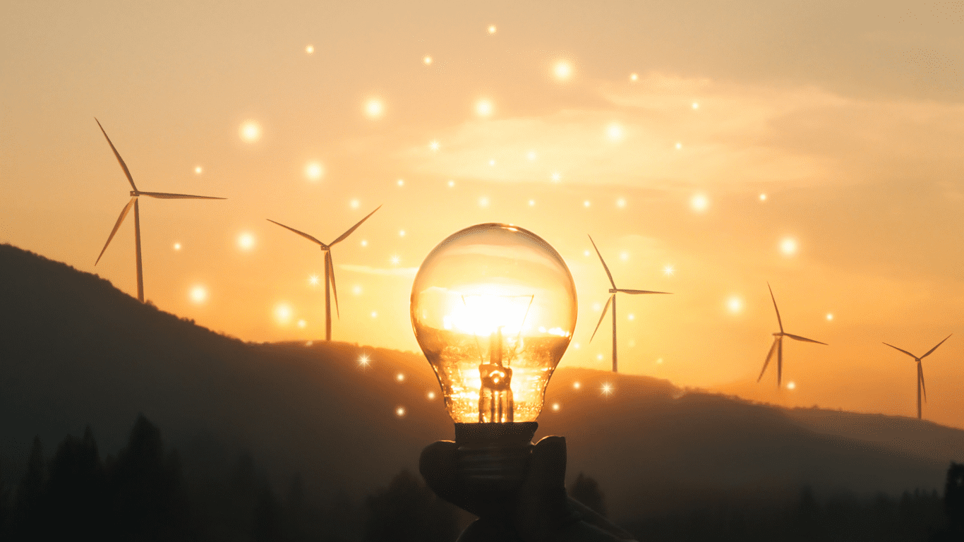 a person holding up a light bulb with wind turbines in the background